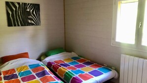A small room with two beds, each with a colorful quilt, a zebra print artwork on the wall, and a window with natural light. - Atypical chalet, calm nature and river (Hautecourt-Romanèche)