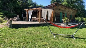 A rustic wooden cabin with a covered outdoor seating area, a hammock, and a small garden. - Atypical chalet, calm nature and river (Hautecourt-Romanèche)
