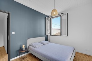 Un dormitorio con una cama, una lámpara de noche y una ventana con un persiano abierto.
