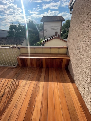 A wooden deck with a built-in bench, a metal railing, and a view of a house in the background.