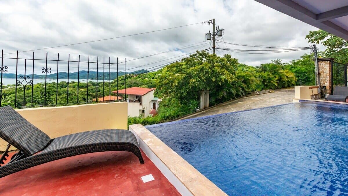 Una piscina con vista a un paisaje montañoso, una silla roja y un muro de piedra.