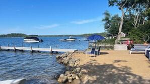 A lakeside beach with a dock, boats, and beach chairs. - Waterfront lake house  private beach dock (harwich)