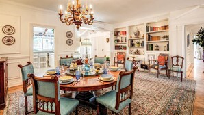Ein Esszimmer mit einer Chandelierleuchtre, Holzstühlen, einem runden Tisch, gedeckt für sechs Personen, und einem gemusterten Teppich.