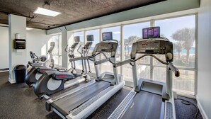 A gym with treadmills, exercise bikes, and a rowing machine, with large windows offering a view of the outdoors.