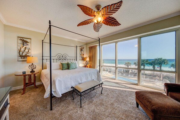 A four-poster bed with a view of the beach, a ceiling fan, and a large window.