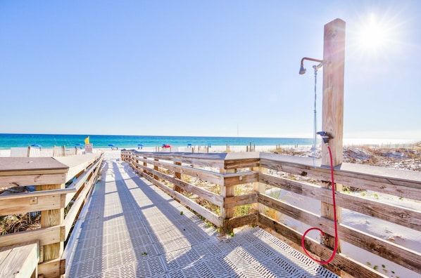 A wooden boardwalk leading to a beach with a wooden structure and a red hose.