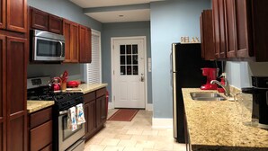 A kitchen with wooden cabinets, a stainless steel microwave, a black refrigerator, and a granite countertop.