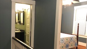 A staircase with white balusters leading to a room with a bed and a window with blinds.