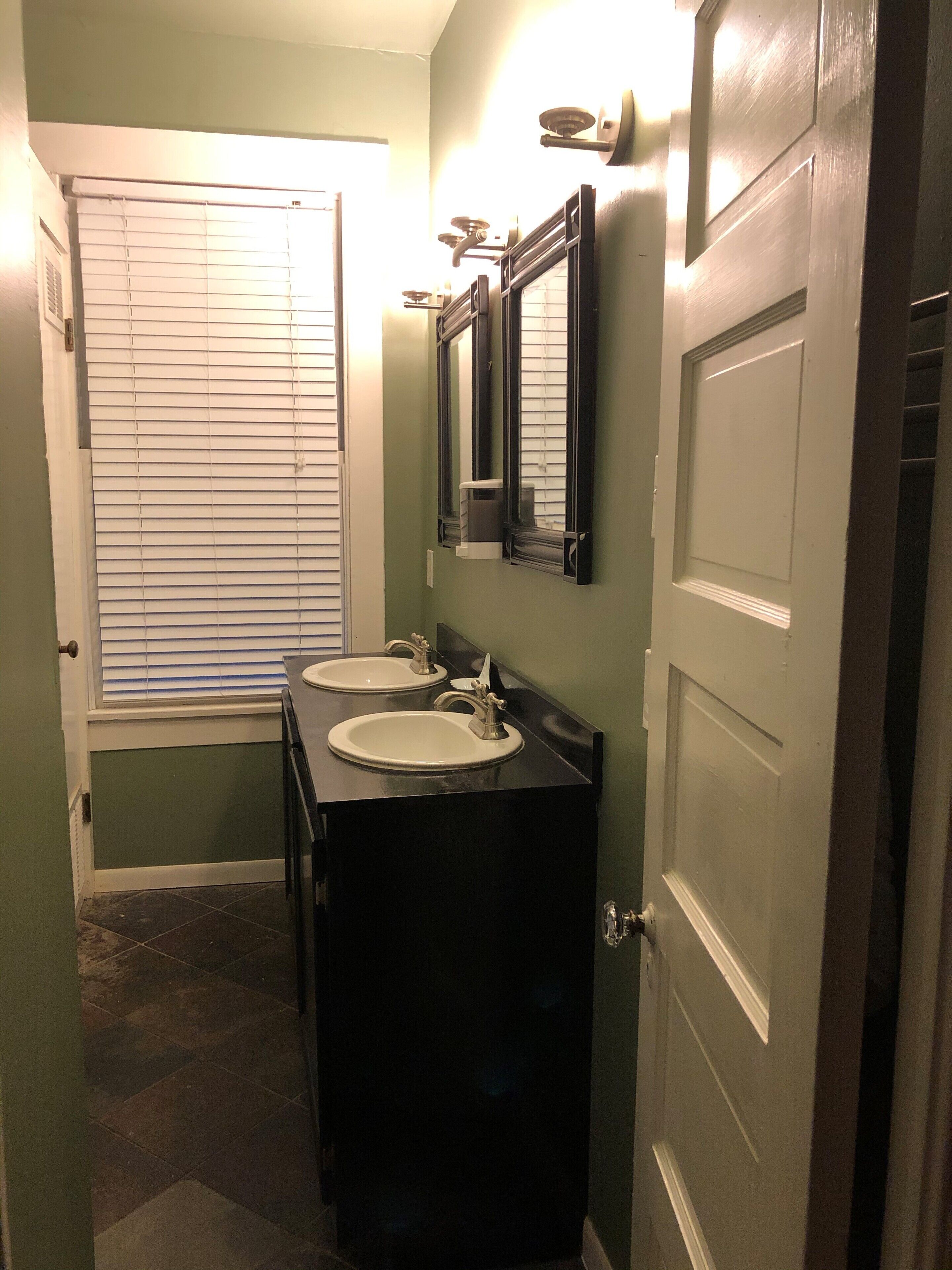 Un baño estrecho con dos lavamanos, un espejo y una puerta.
