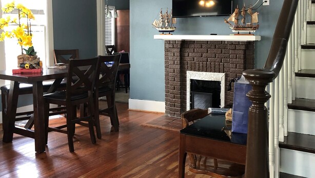 A dining area with a wooden table and chairs, a fireplace with a TV above it, and a staircase with a wooden railing.