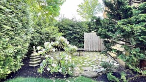 Un jardin avec une clôture en bois, une sculpture en pierre et divers arbustes.