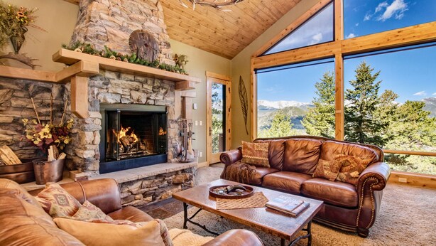 Un salon chaleureux avec une cheminée en pierre, des meubles en cuir et une grande fenêtre donnant sur une vue imprenable sur les montagnes.