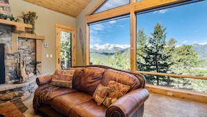 Un salon chaleureux avec un canapé en cuir, une cheminée en pierre et une grande fenêtre donnant sur une vue imprenable sur les montagnes.
