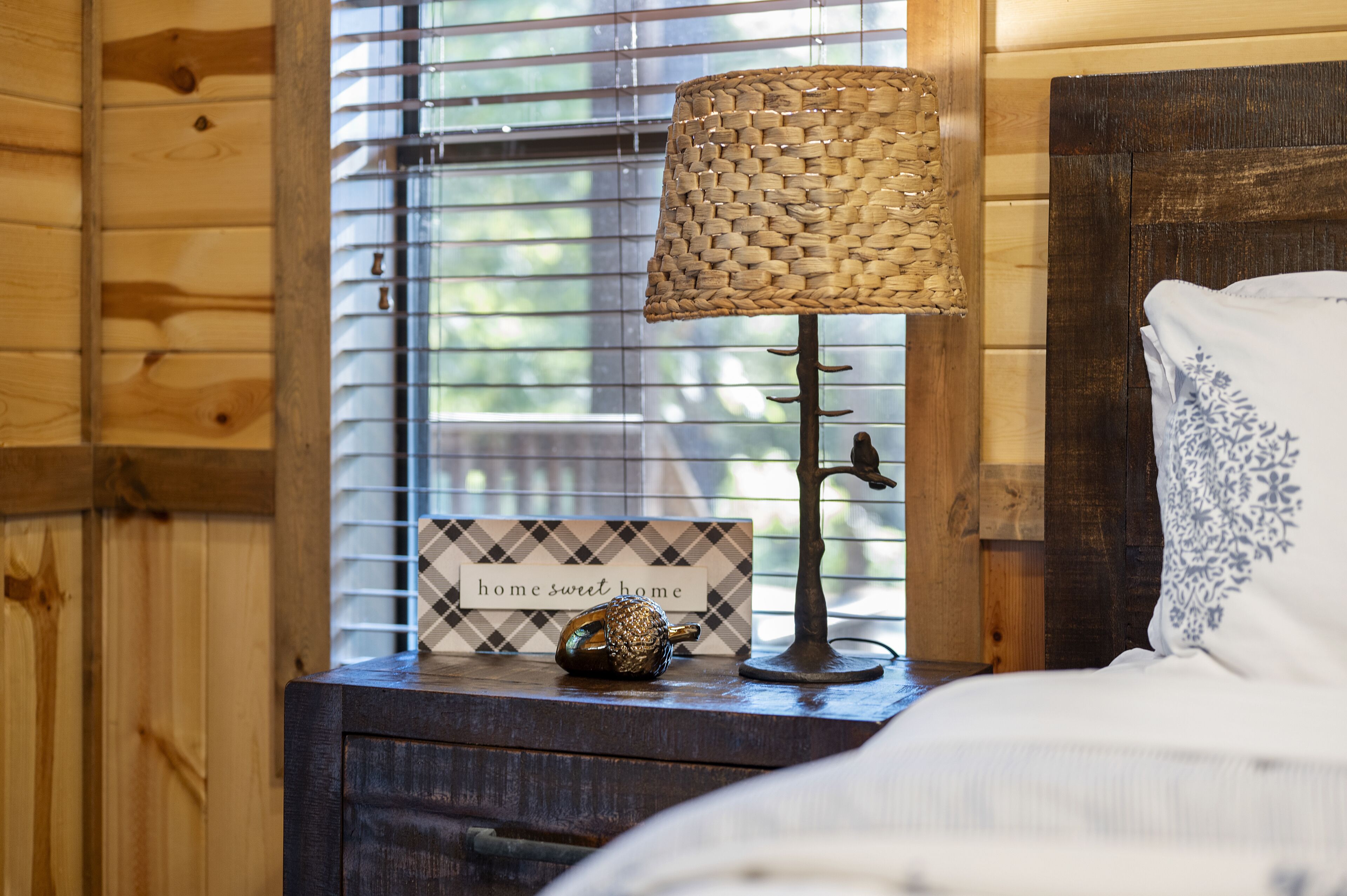 A wooden cabin interior with a bed, a lamp, a decorative item, and a sign reading "home sweet home."