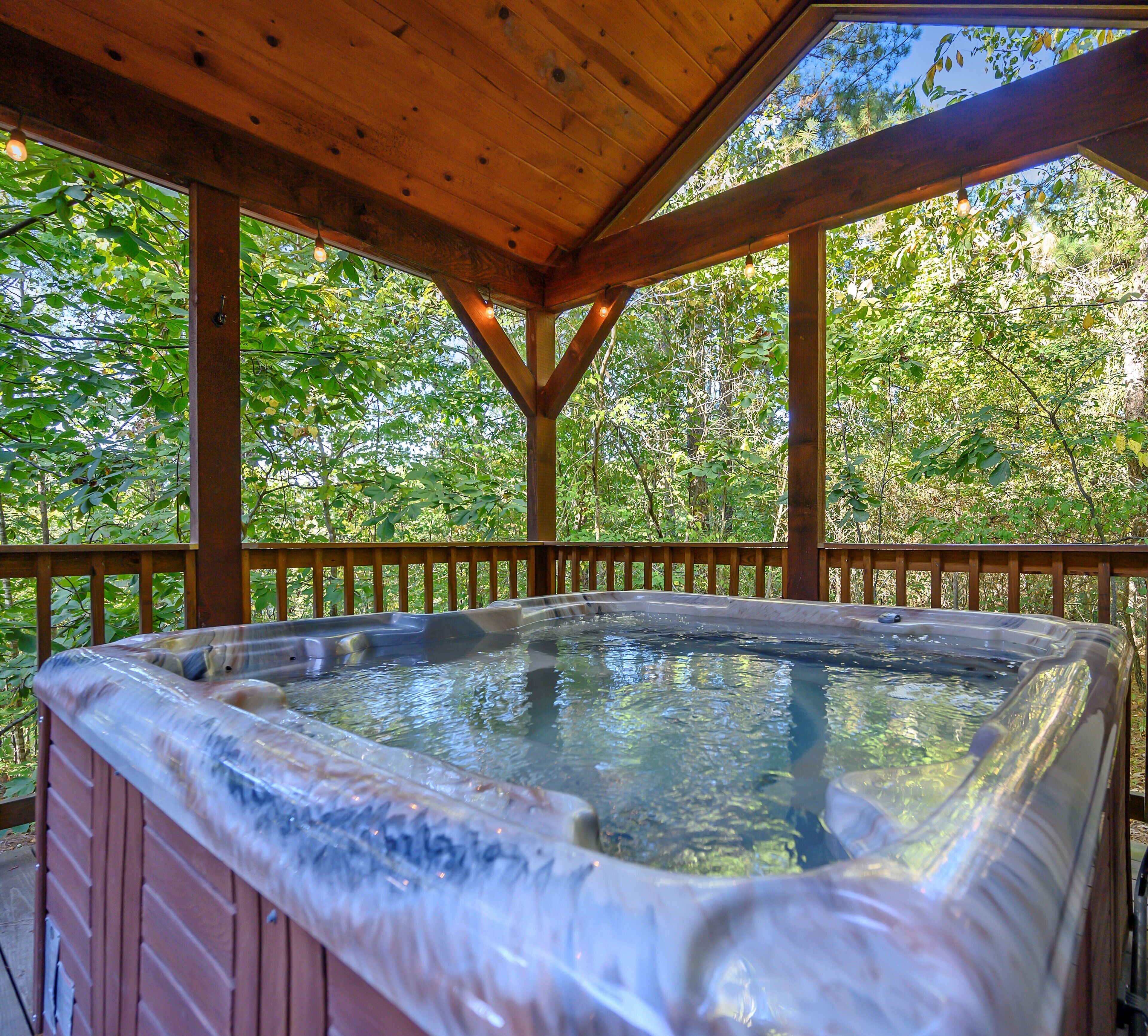 A hot tub under a wooden pergola with a natural backdrop of trees.