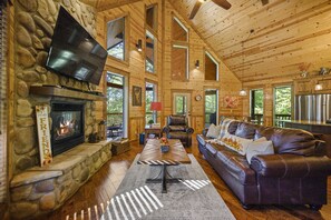 A cozy cabin interior with a stone fireplace, leather sofa, and a flat-screen TV mounted on the wall. - 2,000 sqft, 2 Spacious King Suites & Bunk Room (Broken Bow)