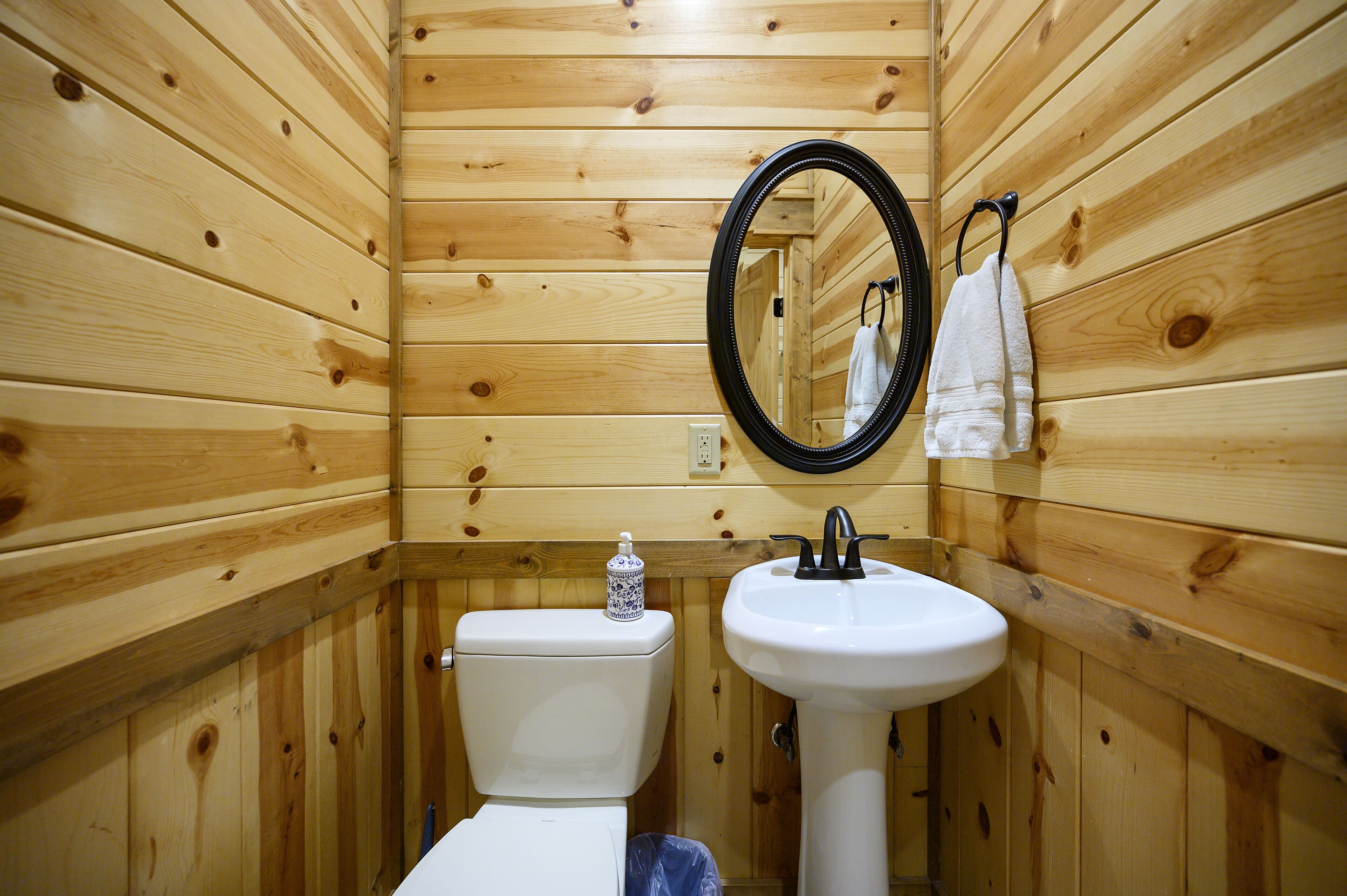A wooden-paneled bathroom with a toilet, sink, and mirror.