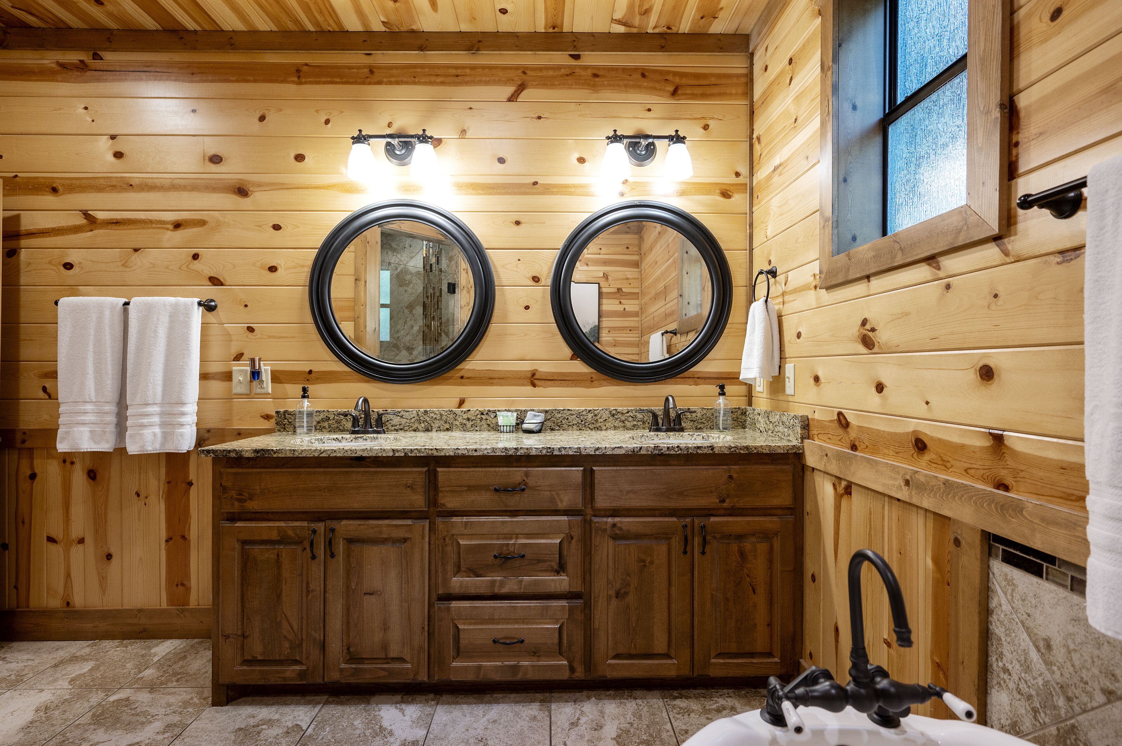 A wooden cabin bathroom with two sinks, wooden cabinets, and a large mirror.