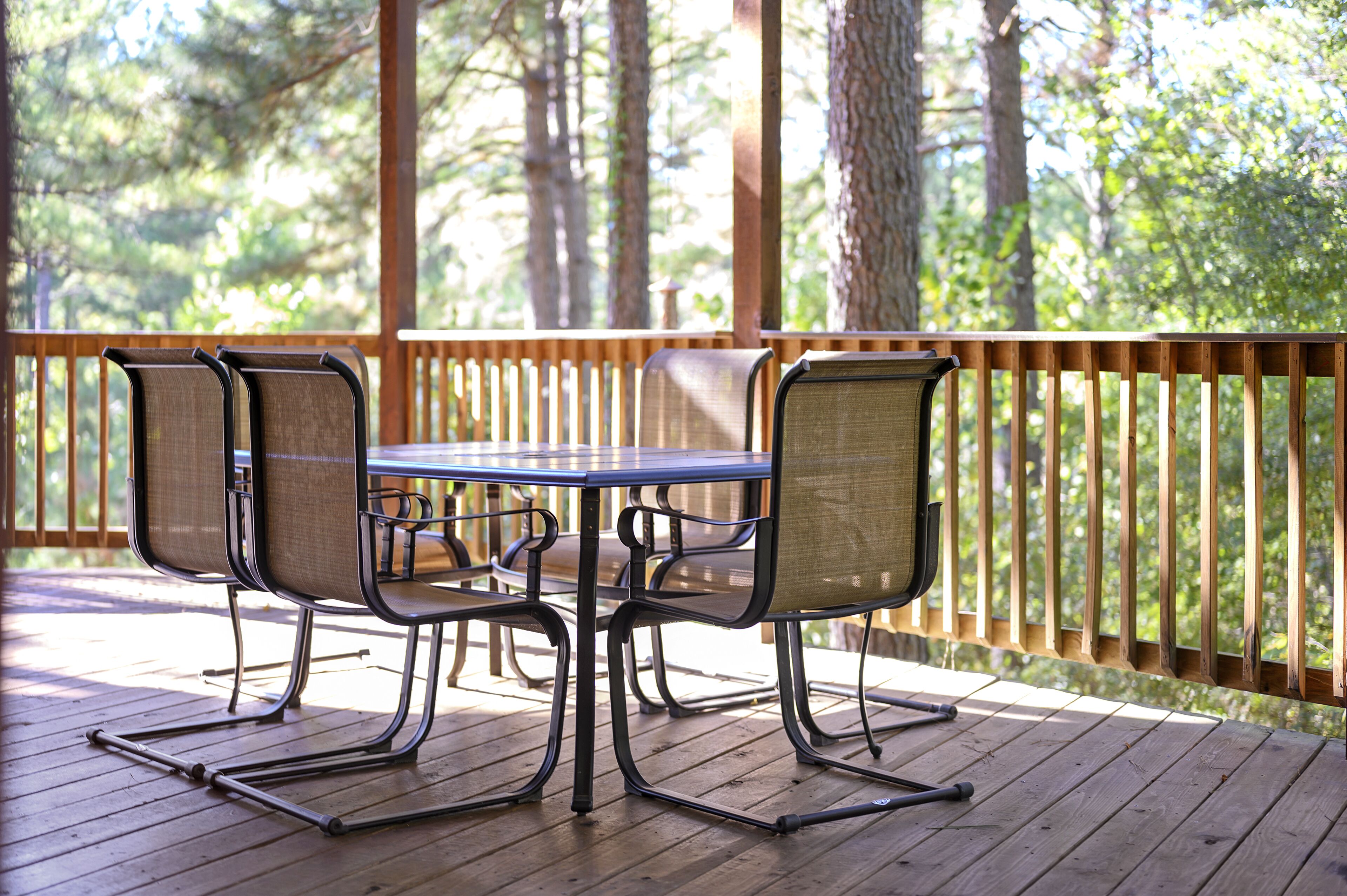 A wooden deck with a table and chairs, surrounded by a wooden railing, overlooking a forested area.