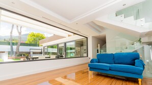 A modern living room with a blue sofa, large windows, and a wooden floor.