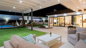 A modern outdoor living area with a pool, a covered patio, and a dining area.