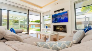 A modern living room with a large sofa, a glass coffee table, and a fireplace.