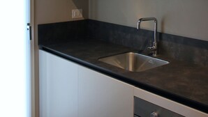 Una cocina moderna con encimera negra, pileta de acero inoxidable y muebles blancos.