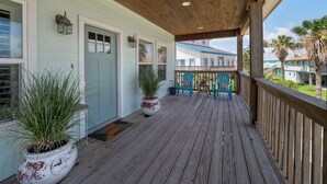 Eine Holzterrasse mit Blumentöpfen, einer Fußmatte und zwei Stühlen.