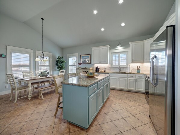 A spacious kitchen with a central island, white cabinetry, and a stainless steel refrigerator.