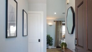 Um corredor com porta branca, quadros, planta em vaso e espelho na parede.