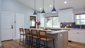 Cozinha moderna com ilha central, iluminação pendente e vista para o exterior.