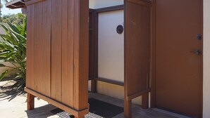 Uma estrutura de madeira ao ar livre, com porta, possivelmente um depósito ou um pequeno espaço, ao lado de um edifício com porta marrom.