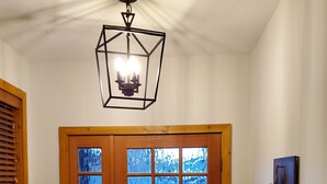 Een houten voordeur met glaspanelen, een trap met houten leuningen, een wandlamp en een kunstwerk aan de muur.
