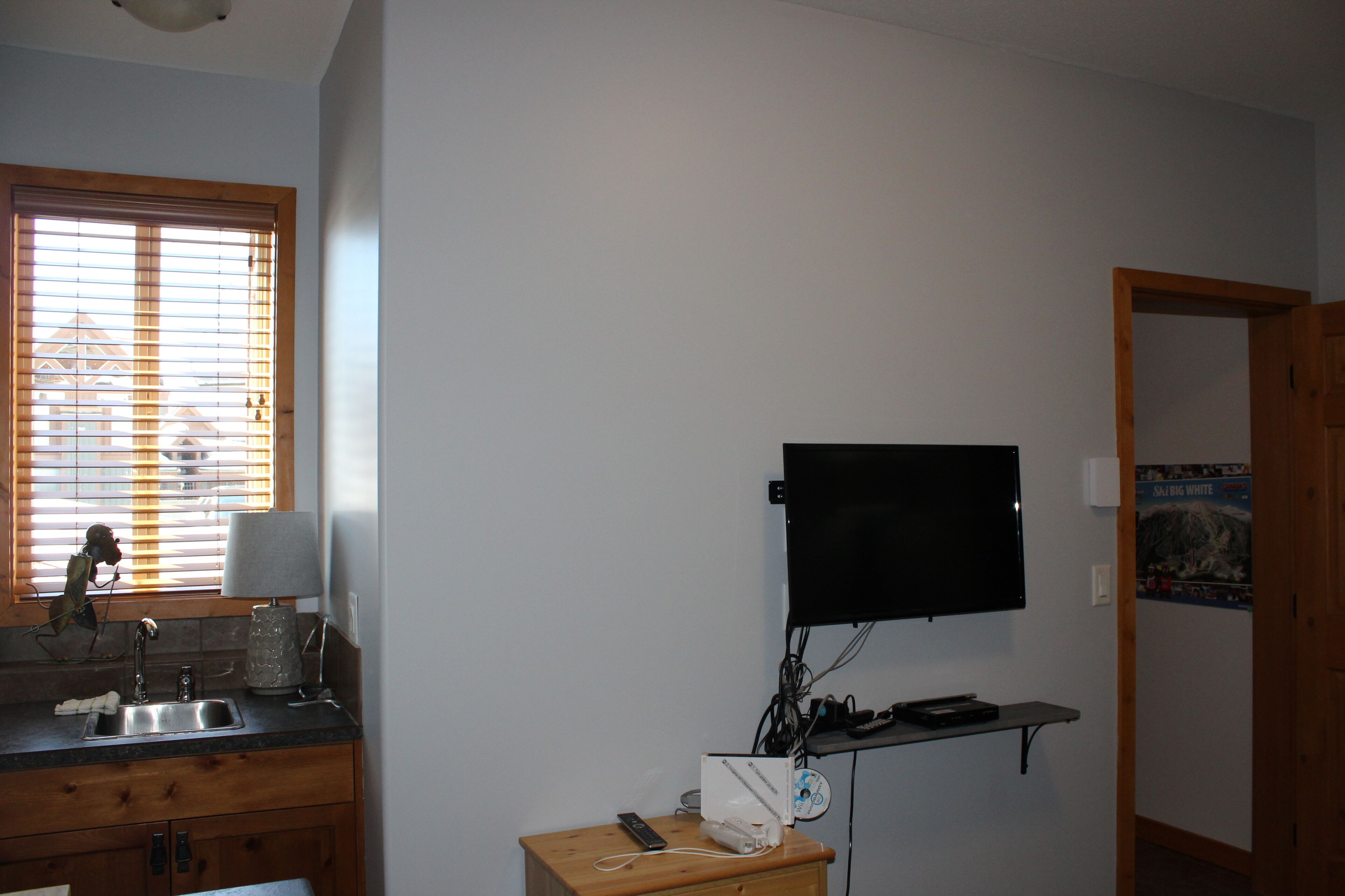 Eine Küche mit Spüle, einem Fenster mit Jalousien, einem an der Wand montierten Fernseher und einem kleinen Holztisch.
