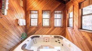 Een houten chalet met een bubbelbad, houten wanden en drie ramen.