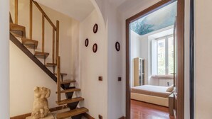 A staircase with wooden steps and a marble floor, leading to a bedroom with a bed and a window.
