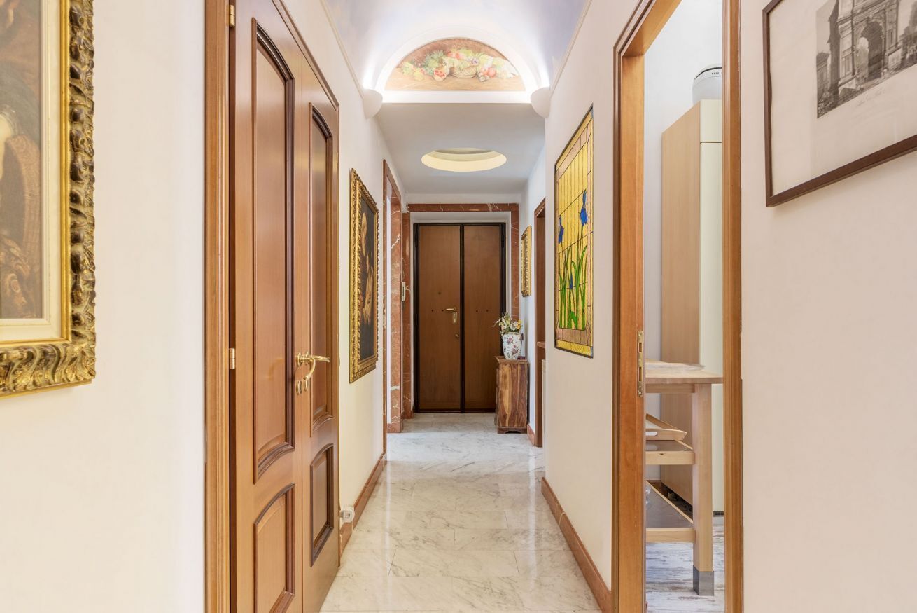 Un couloir avec des portes en bois, des œuvres d’art encadrées et un plafond doté d’une lucarne.