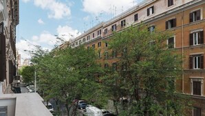 A multi-story building with a row of parked cars and trees in front.