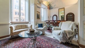 A room with a sofa, armchairs, a glass coffee table, and a patterned rug.