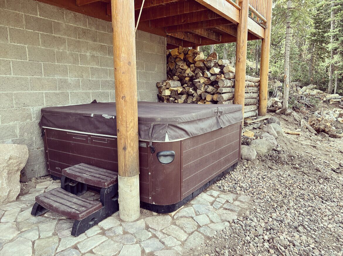 A hot tub with steps, a brick wall, and a pile of firewood.