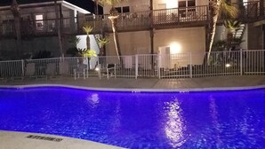 A swimming pool with a blue tint, surrounded by a white fence and palm trees.