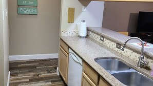 A kitchen with wooden cabinets, a granite countertop, a dishwasher, and a paper towel dispenser.