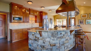 A kitchen with wooden cabinets, a stone island, and a large range hood. - Stewart Highlands Vacation Home at Windcliff (Estes Park)