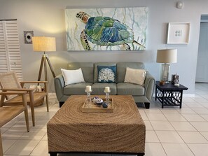 Un salon avec un canapé gris, une table basse en bois, une lampe et une œuvre d’art encadrée représentant une tortue de mer.