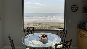 Un coin repas avec une table et des chaises en verre, une vue sur la plage et un ventilateur de plafond.