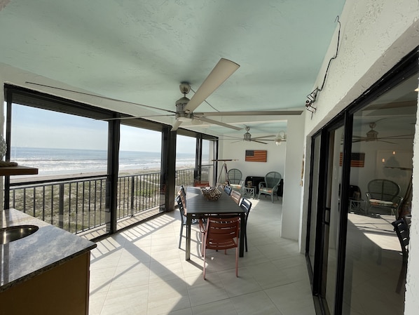 Un balcon avec vue sur la plage, un ventilateur de plafond et une table avec des chaises.
