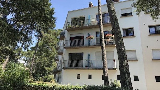 Ein mehrstöckiges Wohnhaus mit Balkonen, umgeben von Bäumen und Grünflächen.