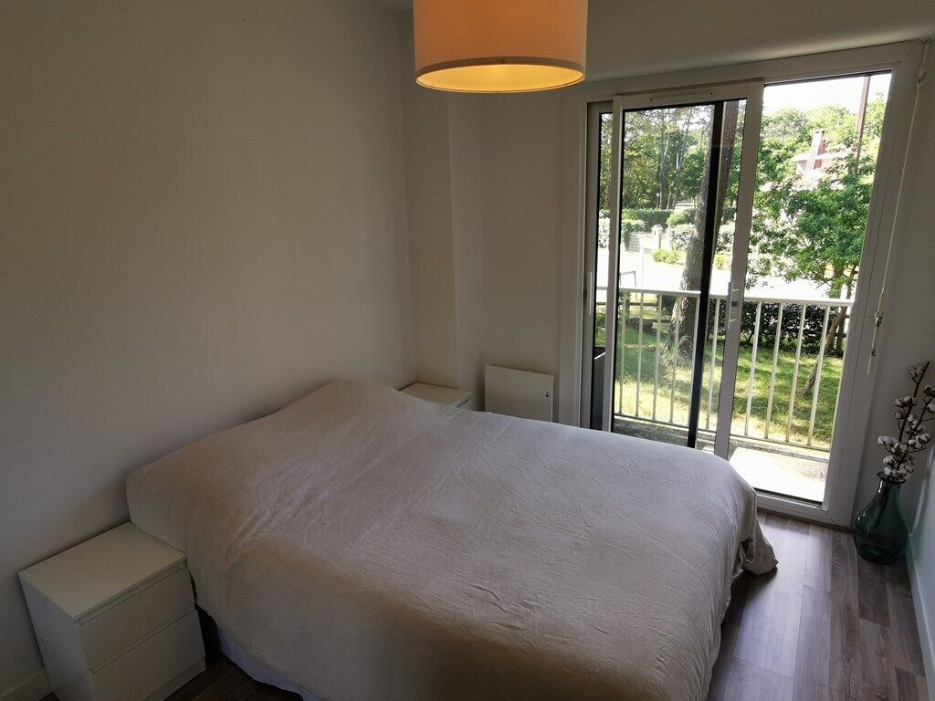 Une chambre à coucher comprenant un lit, une table de chevet, une fenêtre donnant sur un espace verdoyant et une porte menant à un balcon.