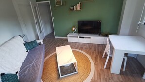 Ein modernes Wohnzimmer mit Fernseher, einem weißen Schreibtisch und einer Couch.