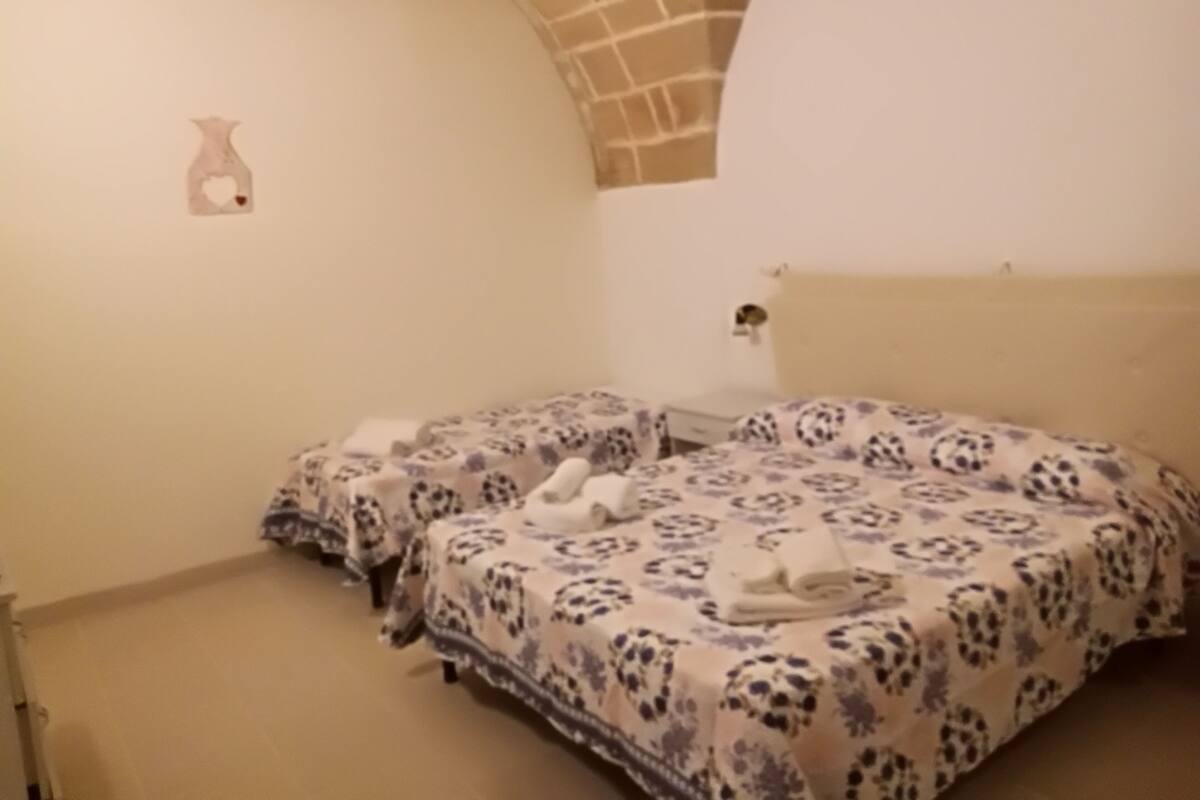 Ein Schlafzimmer mit zwei Betten, einem Ziegelbogen, einer kleinen Vase an der Wand und einem Nachttisch mit Lampe.